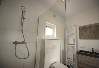 Moderne badeværelse med bruser, toilet, vask og håndklæder i Dune Lodge de Luxe på Camping Zonneweelde.