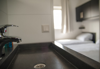 Modern sink and faucet with a view of a bright bedroom at Dune Lodge de Luxe, Camping Zonneweelde, Netherlands.