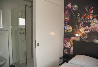Moderne lodge med glasbruser, hvide fliser, skydedør og blomstret accentvæg hos Camping Zonneweelde.