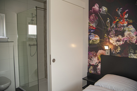 Moderne lodge met glazen douche, schuifdeur en bloemrijke accentmuur bij Camping Zonneweelde.