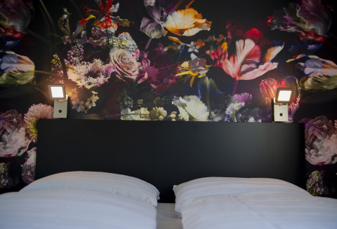Bett mit weißer Bettwäsche, schwarzem Kopfteil und bunter Blumenwand in Dune Lodge de Luxe, Zonneweelde.