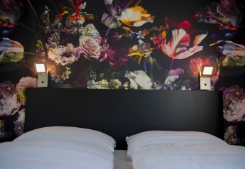 Cama con sábanas blancas y cabecero negro ante mural floral en Dune Lodge de Luxe, Camping Zonneweelde.