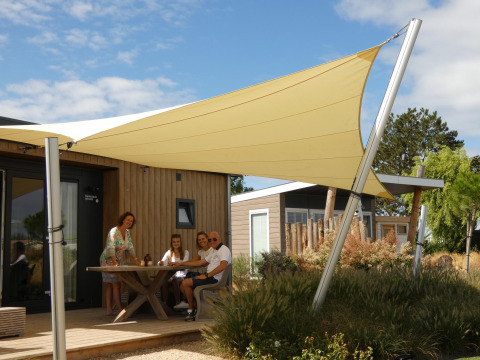 Famiglia seduta all’aperto presso Dune Lodge de Luxe a Camping Zonneweelde, Olanda, sotto tenda parasole.
