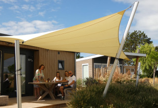 Gezin onder schaduwdoek bij Dune Lodge de Luxe op Camping Zonneweelde, Nederland, genietend van buiten.
