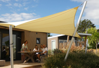 Famiglia seduta all’aperto presso Dune Lodge de Luxe a Camping Zonneweelde, Olanda, sotto tenda parasole.