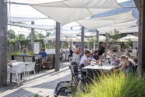 Buitenterras van Dune Lodge de Luxe, Camping Zonneweelde, Nederland, met etende gasten en bediening.