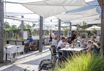 Udendørs terrasse på Dune Lodge de Luxe, Camping Zonneweelde, Holland, med gæster og servering.