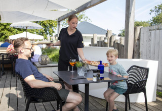 Een serveerster brengt pizza naar een vader en zoon die buiten eten bij Dune Lodge de Luxe.