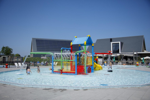 Kinderen genieten van een kleurrijke waterspeeltuin bij een lodge, met glijbanen en waterstralen.