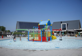 Kinderen genieten van een kleurrijke waterspeeltuin bij een lodge, met glijbanen en waterstralen.