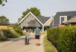 Een man wandelt met een kind op de fiets voor de Dune Lodge de Luxe bij Camping Zonneweelde in Nederland.