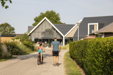 Een man wandelt met een kind op de fiets voor de Dune Lodge de Luxe bij Camping Zonneweelde in Nederland.