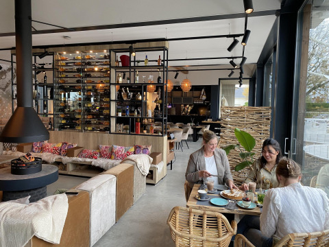 Tres mujeres disfrutan de comida y bebida en una acogedora lodge moderna con decoración elegante y luz natural.