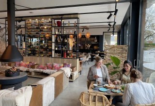 Tres mujeres disfrutan de comida y bebida en una acogedora lodge moderna con decoración elegante y luz natural.