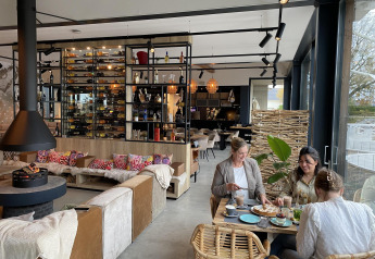 Tres mujeres disfrutan de comida y bebida en una acogedora lodge moderna con decoración elegante y luz natural.