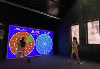 Due persone giocano a un gioco a punti su uno schermo interattivo in un lodge moderno con tema sportivo.