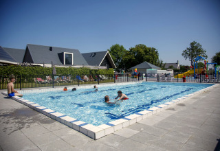 Piscine extérieure dans un lodge avec enfants, adultes et aire de jeux sous un beau soleil d’été.