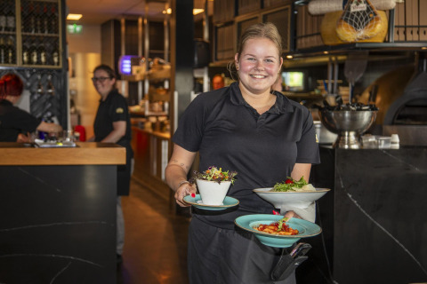 Vriendelijke serveerster met gerechten in Dune Lodge de Luxe op Camping Zonneweelde, Nederland, restaurant.