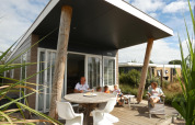 Familia disfrutando en la terraza del Beach Loft + Wellness en Camping Zonneweelde, Países Bajos, día soleado.