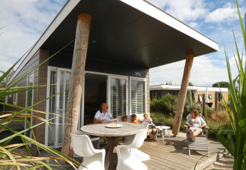 Familia disfrutando en la terraza del Beach Loft + Wellness en Camping Zonneweelde, Países Bajos, día soleado.