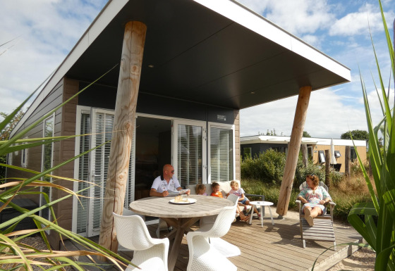 Gezin aan het relaxen op het terras bij Beach Loft + Wellness op Camping Zonneweelde, Nederland, zonnig weer.