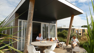 Familie genießt die Sonne auf der Terrasse des Beach Loft + Wellness am Camping Zonneweelde, Niederlande.
