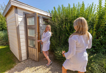 Zwei Frauen in Bademänteln vor einer Sauna bei Beach Loft + Wellness auf Camping Zonneweelde, Niederlande.