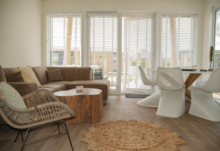 Soggiorno moderno al Beach Loft + Wellness di Camping Zonneweelde, Paesi Bassi, con grandi finestre e arredamento accogliente.