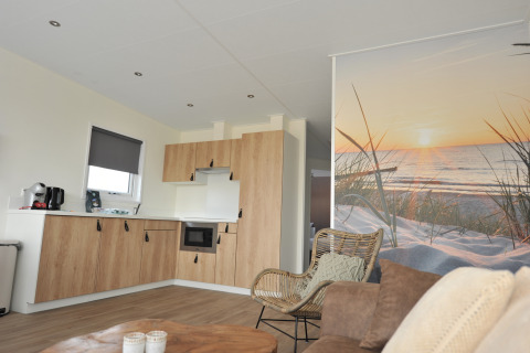 Cocina y sala modernas de una cabaña con mural de playa al atardecer en Camping Zonneweelde, Países Bajos.