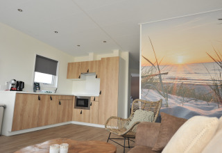Cucina e soggiorno di una lodge moderna con murale tramonto sulla spiaggia a Camping Zonneweelde, Paesi Bassi.