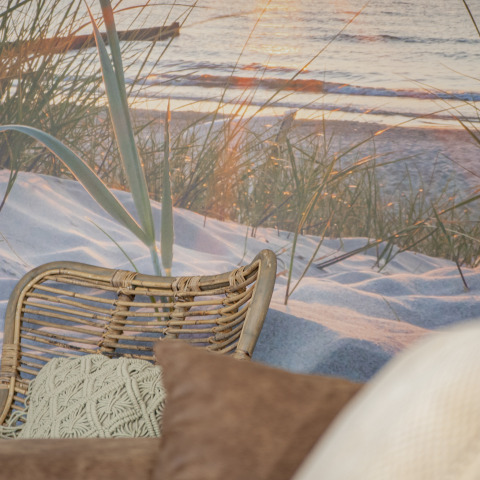 Gemütlicher Sitzbereich mit Rattanstuhl und Kissen vor Strandtapete im Beach Loft von Camping Zonneweelde.