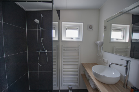 Baño moderno con ducha negra, lavabo redondo, encimera de madera y ventanas en Camping Zonneweelde.