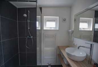 Moderne badeværelse med sort bruseniche, håndvask, træbordplade og små vinduer på Camping Zonneweelde.