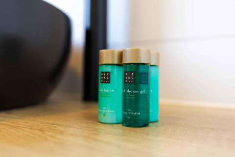 Tres botellas de productos Rituals sobre una superficie de madera en una habitación de lodge luminosa.