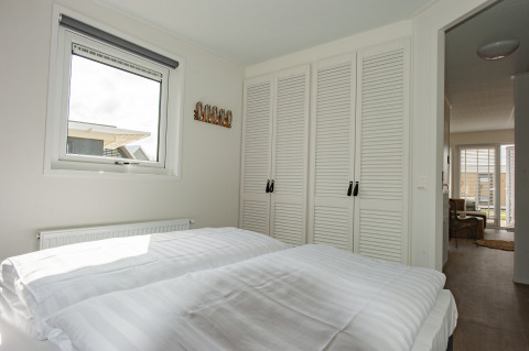 Dormitorio con ropa de cama blanca, armarios empotrados y ventana en Beach Loft + Wellness, Camping Zonneweelde.