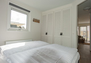 Soveværelse med hvidt sengetøj, garderobeskabe og vindue på Beach Loft + Wellness, Camping Zonneweelde.