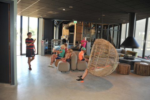 Des enfants se détendent dans le salon moderne d'un lodge avec chaise suspendue et grande fenêtre.
