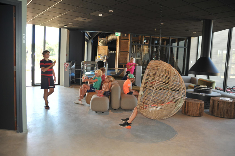 Kinder entspannen sich in der modernen Lodge-Lobby mit Hängesessel und stilvollem Interieur.