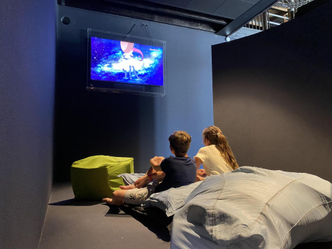 Twee kinderen zitten op kussens in een lodge en kijken naar een tekenfilm op tv in een knus hoekje.