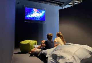 Due bambini sono seduti su cuscini in un lodge e guardano un cartone animato in TV in una stanza accogliente.