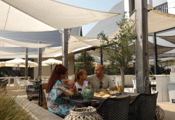 Famille dînant en terrasse sous des voiles d'ombrage à Beach Loft + Wellness, Camping Zonneweelde.