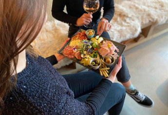Two people at a lodge enjoy a glass of wine and share a charcuterie platter with meats, cheese and olives.