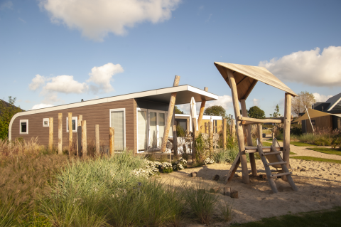 Moderne strandhut met wellness en speelzone bij Camping Zonneweelde in Nederland, zonnige dag.