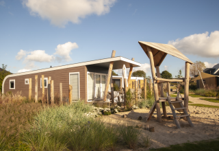 Moderne strandhut met wellness en speelzone bij Camping Zonneweelde in Nederland, zonnige dag.