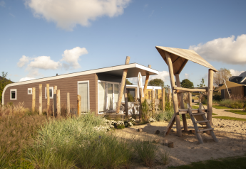 Moderne strandhytte med legeplads og wellness ved Camping Zonneweelde i Holland under blå himmel.