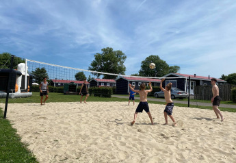 Folk spiller beachvolley foran Beach Loft + Wellness ved Camping Zonneweelde i Holland på en solrig dag.