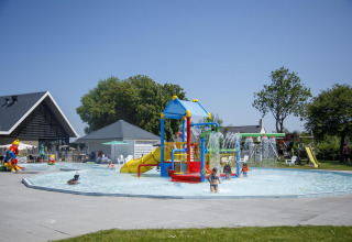 Niños jugando en una piscina exterior poco profunda con toboganes de agua en Camping Zonneweelde, Países Bajos.