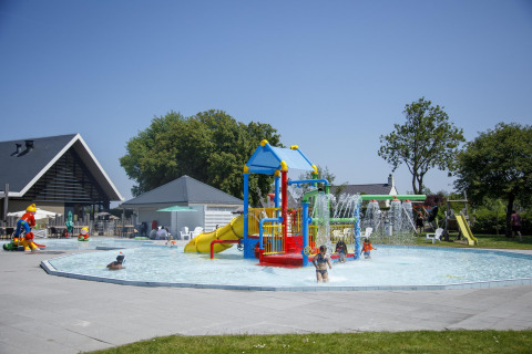 Enfants jouant dans une piscine extérieure peu profonde avec des toboggans colorés à Camping Zonneweelde, Pays-Bas.