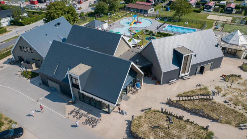 Aerial view of a modern lodge with playground, swimming pool, and bikes set in a landscaped area.