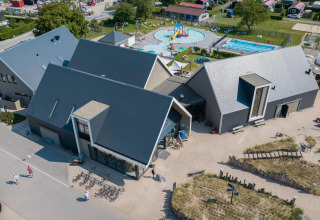 Vista aerea di un lodge moderno con parco giochi, piscina e biciclette, immerso nel verde.